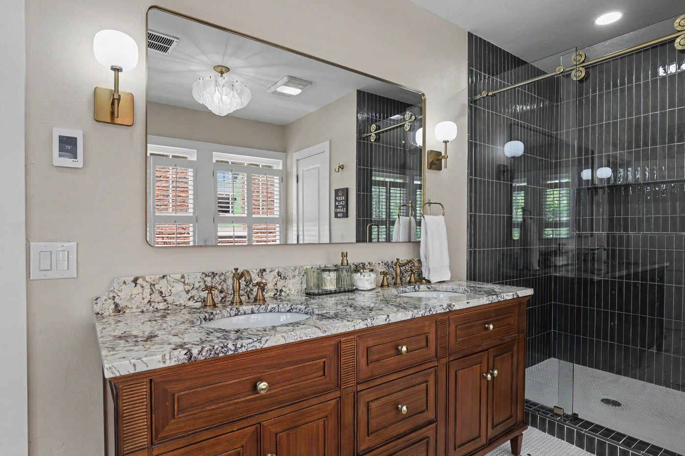Wood double vanity with stone top beside a glass shower
